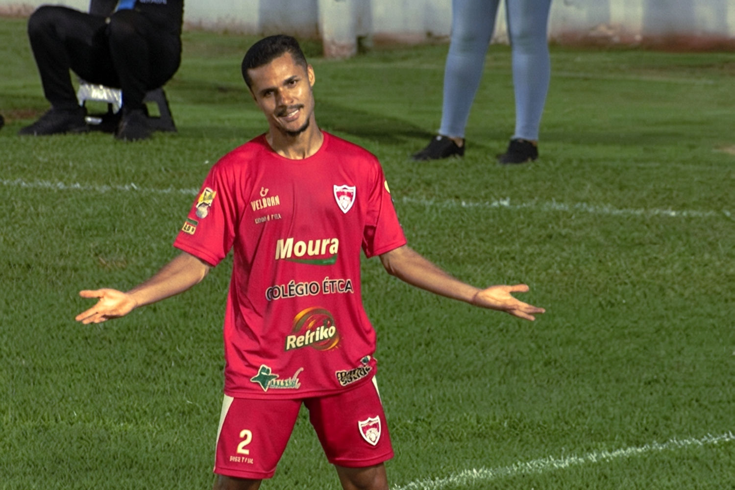 Marquinhos, de braços abertos, com o uniforme principal do City London, todo em vermelho, comemora o gol